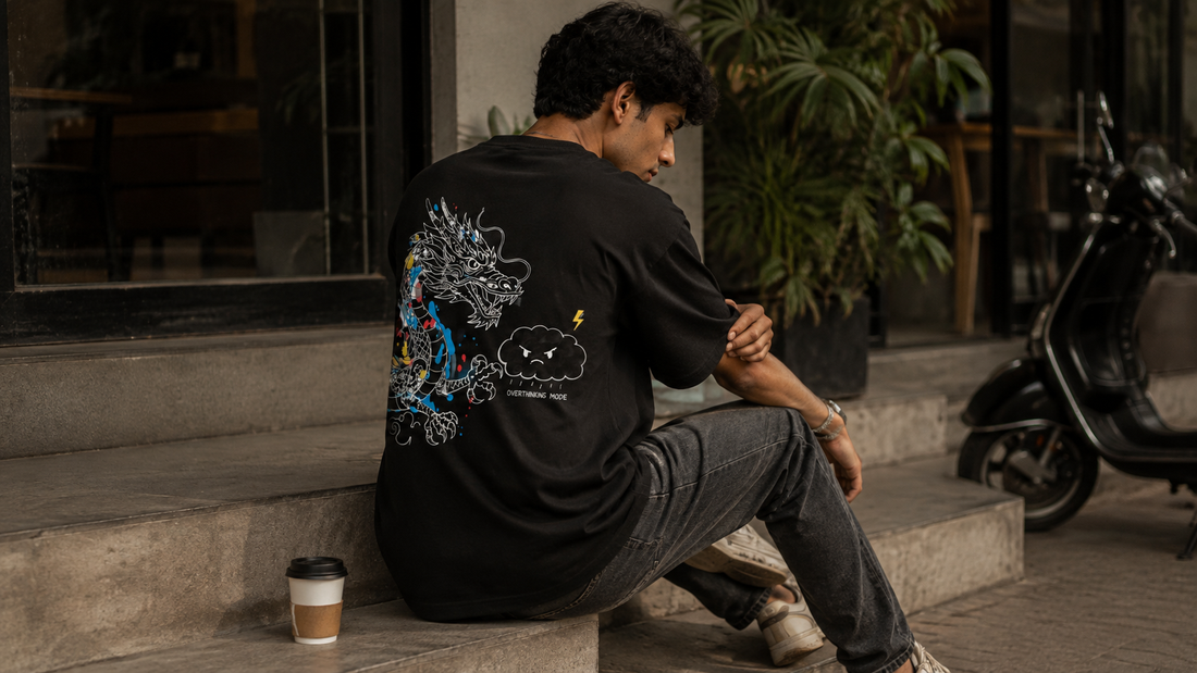 Indian male model wearing LOWW LISTED Overthinking Mode black oversized T-shirt outside an urban cafe